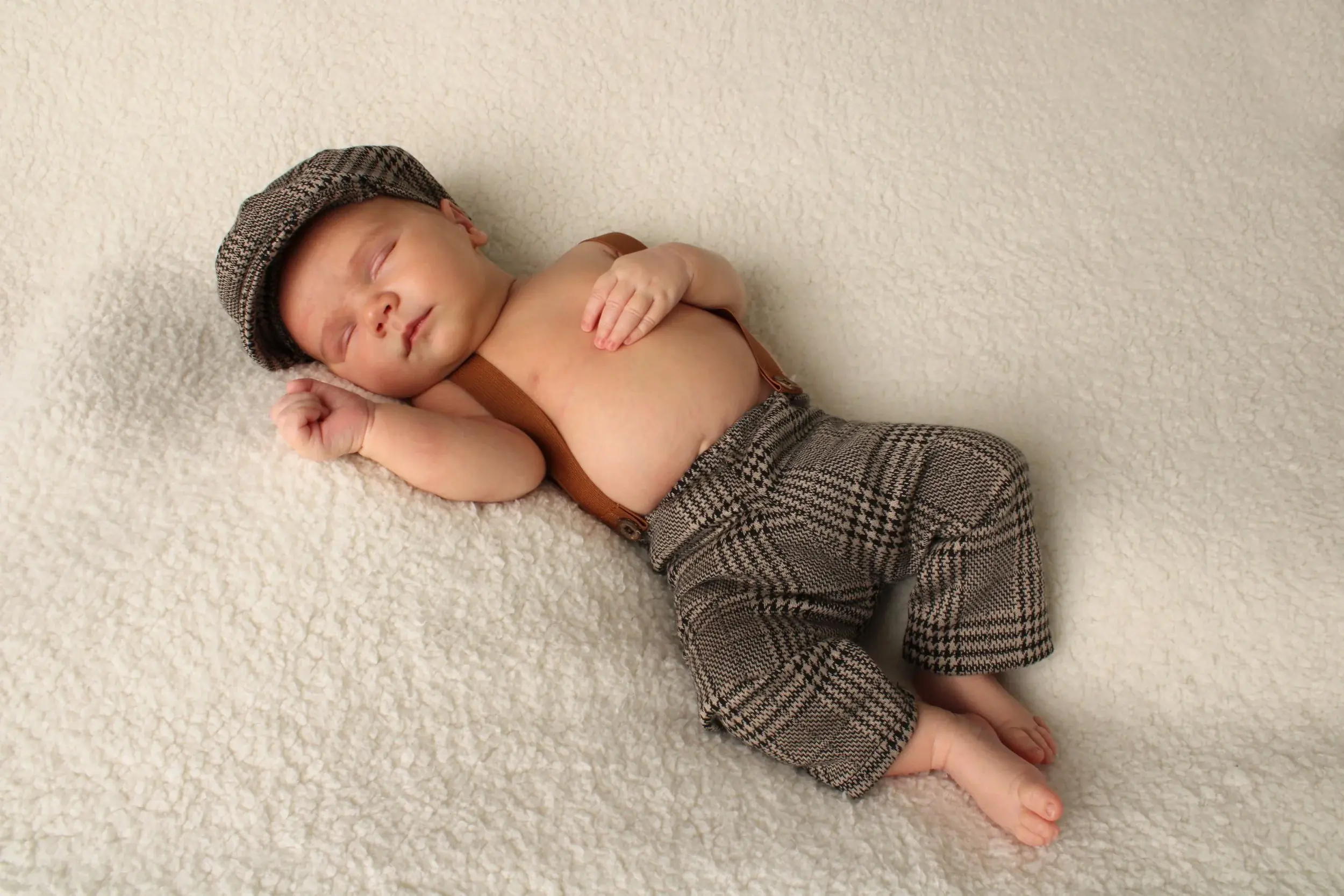 Sleeping newborn baby boy wearing a houndstooth cap and suspenders — serving Baldwin, NY families