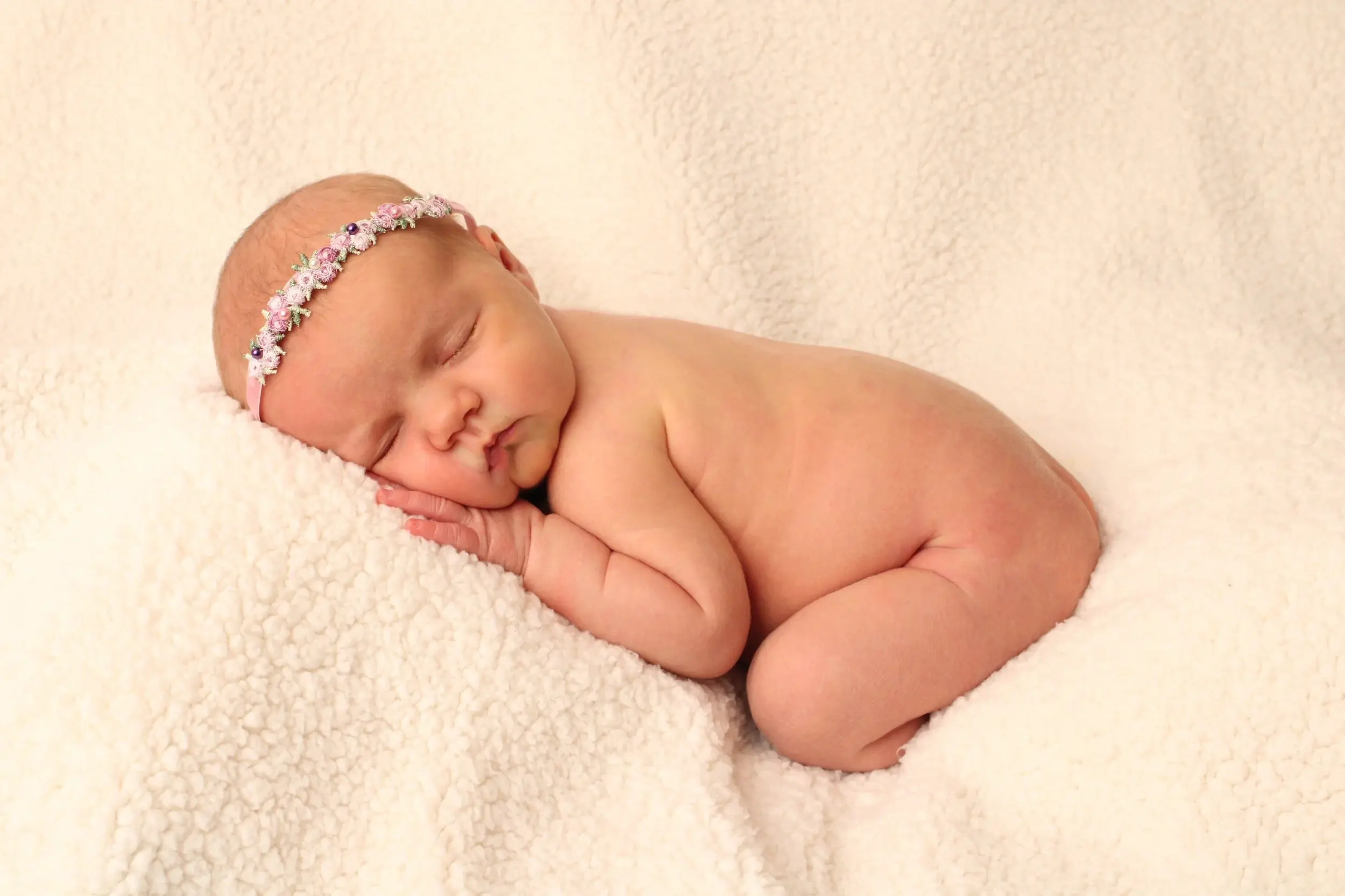 Newborn baby girl wearing a pink floral headband, sleeping on a cream blanket — Long Island newborn and family photography