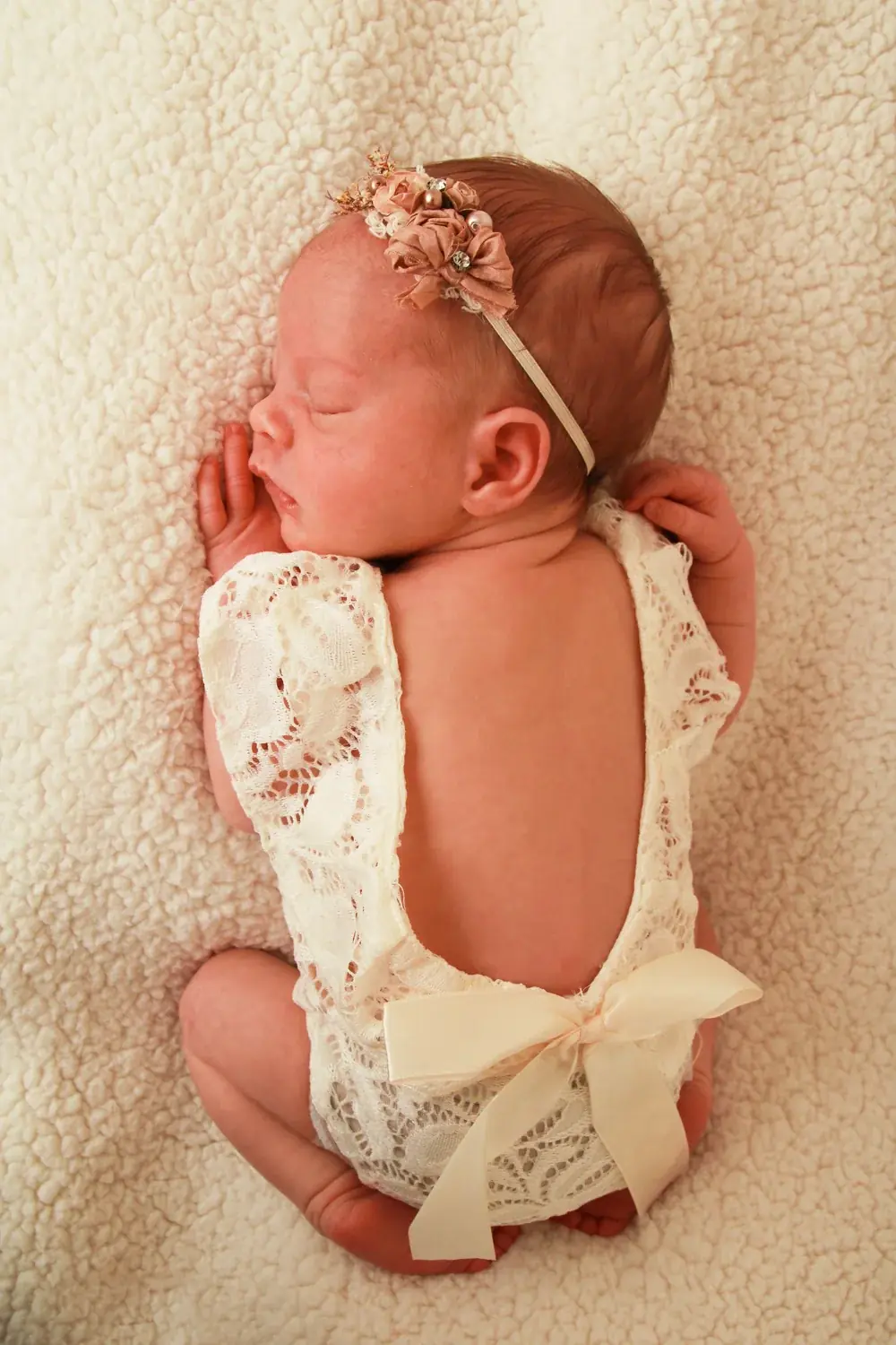 Back view of a newborn baby girl wearing a lace romper with a bow — serving Atlantic Beach, NY families