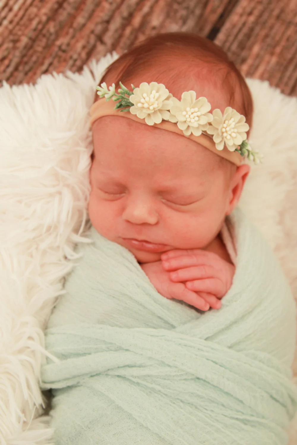 Newborn baby girl swaddled in a mint green wrap with a floral headband — serving Lawrence, NY families