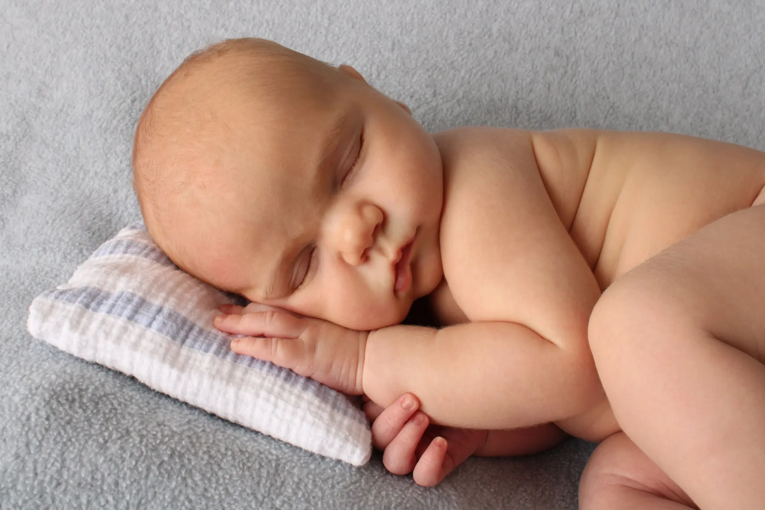 Close-up portrait of a sleeping newborn baby resting on a striped pillow — serving Plainedge, NY families